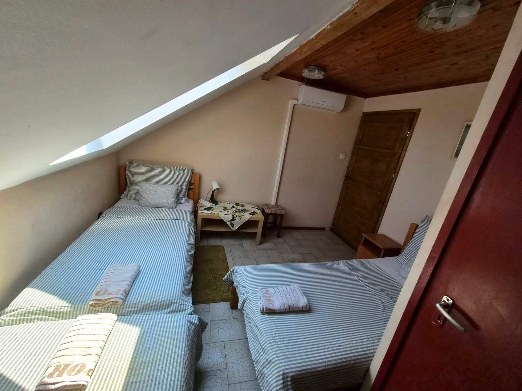 Klímás tetőtéri szoba ágyakkal és fa mennyezettel
